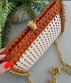 a woman's hand holding an orange and white purse with a gold lion brooch on it