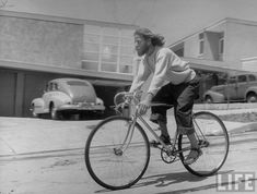 a man riding a bike down a street next to tall buildings with cars parked in the background