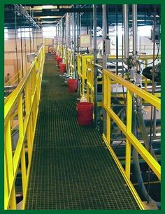 the inside of a factory with yellow railings and red buckets on each side