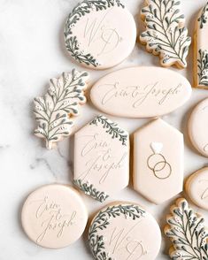 wedding cookies decorated with green leaves and monogrammings on top of a marble table