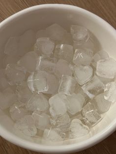 a white bowl filled with ice cubes on top of a wooden table