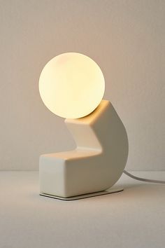 a white lamp sitting on top of a table next to a light bulb in the shape of a wave