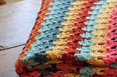 a crocheted blanket is laying on the floor next to a plate and fork