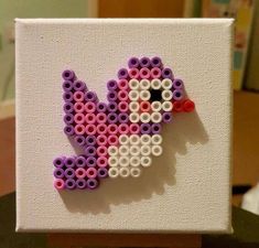 a piece of art made to look like a bird on a white canvas with pink and purple beads