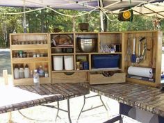 an outdoor kitchen with wooden cabinets and utensils on the counter top under a tent