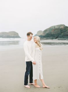 an engaged couple standing on the beach holding hands