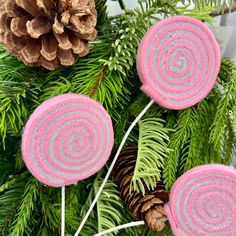 three candy lollipops sitting on top of a pine tree next to a pine cone