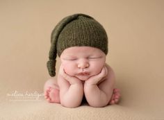 a newborn baby wearing a green hat and laying on its side with his hands under his chin