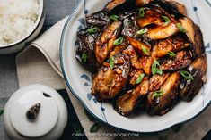 a plate with fried eggplant on it next to a bowl of rice and spoon