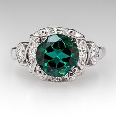 This vintage teal tourmaline ring is centered with one (1) round mixed cut natural tourmaline weighing 2.07 carats that is set into a four-prong setting. The ring is accented with six (6), bead set, round single cut diamonds, bordered with milgrain edging. The ring measures 10.8mm at the top, rises 7.7mm above the finger, tapering to 1.3mm wide and 0.7mm thick at the base of the shank. It is currently a size 6.25. Art Deco Emerald Ring With Accent Stones, Heirloom Emerald Ring With Gemstone Accents For Formal Events, Green Topaz Ring With Center Stone, Elegant Green Topaz Round Cut Ring, Elegant Green Topaz Ring With Round Cut, Elegant Green Topaz Ring, Round Cut, Elegant Green Round Cut Topaz Ring, Green Topaz Ring For Formal Occasions, Art Deco Round Emerald Ring For May Birthstone