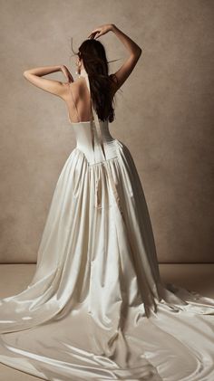 a woman in a white dress with her back to the camera, standing on a beige background