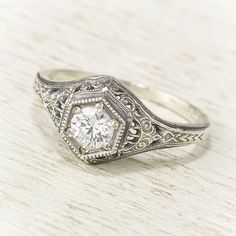 an antique style diamond ring with filigrees on the sides, sitting on a wooden surface