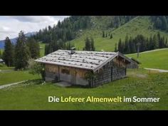 an old wooden cabin in the middle of a green field with trees and mountains behind it