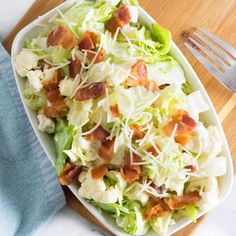 a salad with bacon and lettuce in a white bowl on a wooden cutting board