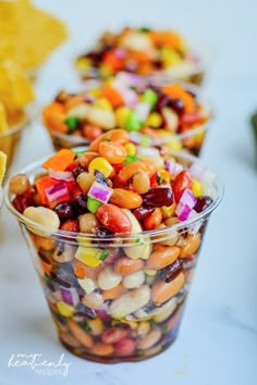 several small bowls filled with different colored candy beans and corn kernels next to chips