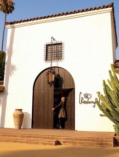 a woman is standing in the doorway of a white building with cactus and potted plants