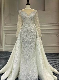 a white wedding dress with long sleeves and beading on the skirt is sitting on a mannequin