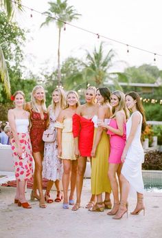 a group of women standing next to each other in front of a pool and palm trees