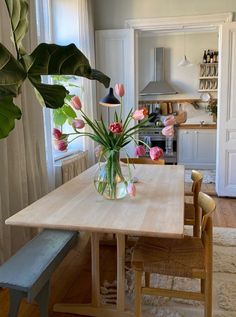 a vase with flowers on top of a wooden table next to a bench in a kitchen