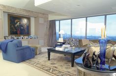 a living room filled with furniture next to large window covered in curtains and windows overlooking the city