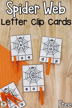 four spider web letter clip cards on a wooden surface with orange ribbon and scissors in front of them