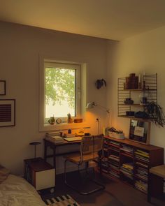 a room with a desk, bookshelf, and lamp in the corner near a window