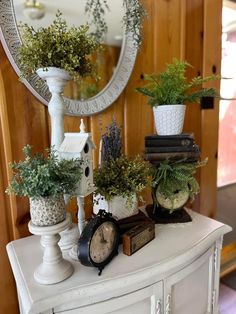 a white dresser topped with potted plants next to a mirror