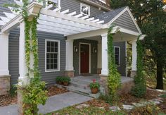 a gray house with white trim and green vines on the front porch, along with potted plants