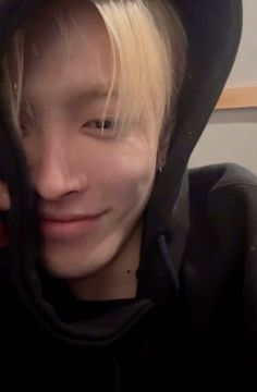 a young man with blonde hair wearing a black hoodie and looking at the camera