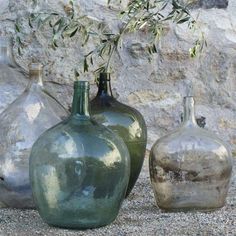 three different colored vases sitting in front of a rock wall with an olive tree