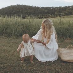 a woman in white dress holding a baby's hand while sitting on the ground