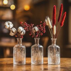 three glass vases with flowers in them sitting on a wooden table next to each other