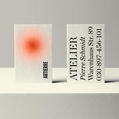 two business cards sitting on top of a white surface with an orange dot in the middle