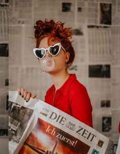 a woman wearing sunglasses and blowing bubbles while holding a newspaper in front of her face