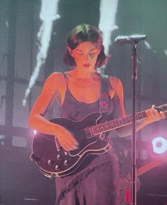 a woman holding a guitar while standing in front of a microphone