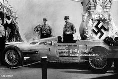 an old race car with men in uniform standing around it and another man looking on