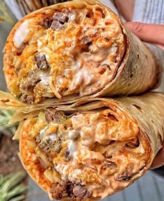 two burritos with meat and cheese on them are held by someone's hand