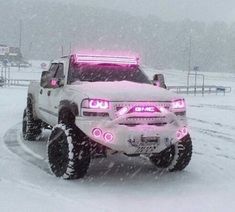 a white truck with pink lights driving down a snow covered road in the middle of winter