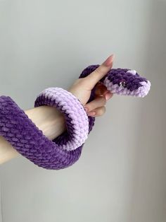 a hand holding a purple and white knitted snake with it's mouth open