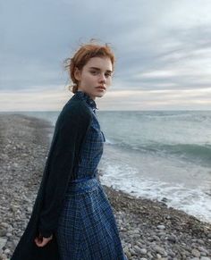 a woman in a blue dress standing on rocks near the ocean and looking at the camera