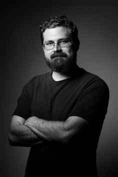 a man with glasses and a beard is posing for a black and white photo in front of a dark background