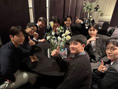 a group of people sitting at a table giving the thumbs up sign with flowers in front of them