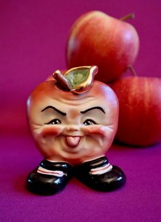 an apple and two apples on a purple background with a small figurine in the foreground