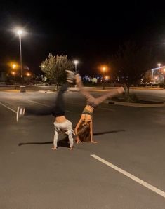 two people doing handstands in the middle of a parking lot at night time