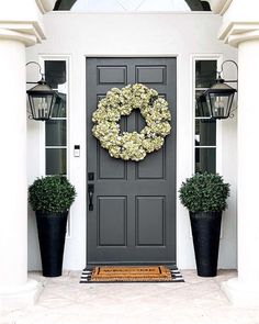 a gray front door with two black planters and a wreath hanging on the side