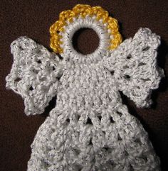 a crocheted angel ornament with yellow and white trim on brown background