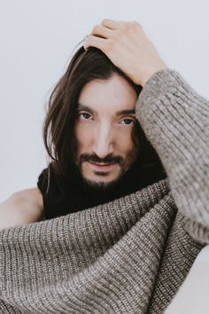 a man with long hair and a goatee is holding his sweater over his head