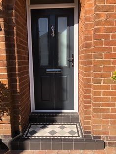 a black front door with a checkered tile floor and sidelight on the brick building