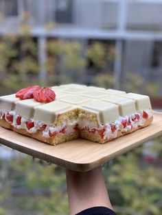 someone is holding up a cake with strawberries on it and white frosting in the middle