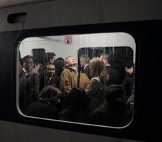 a group of people standing next to each other on a subway train, looking out the window